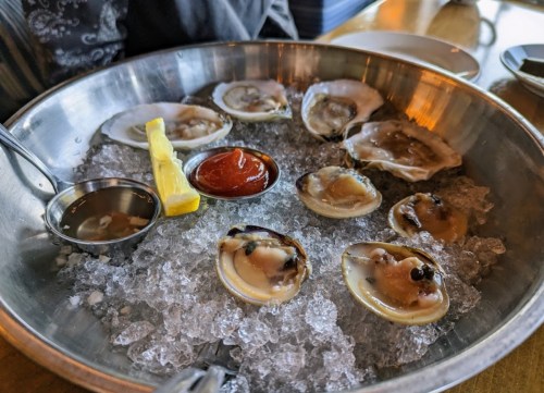 A metal platter filled with oysters on ice, accompanied by lemon and dipping sauces.
