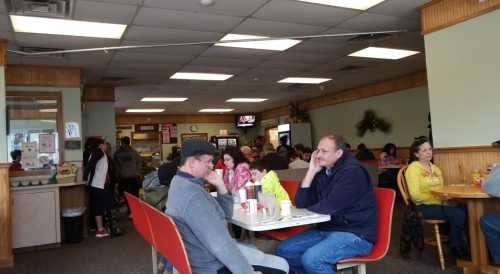 A busy diner with patrons seated at tables, some chatting, and a counter in the background. Warm, casual atmosphere.