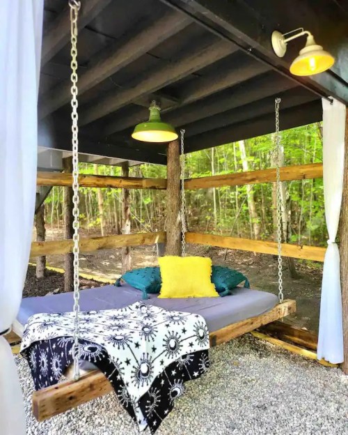 A cozy swing bed with pillows and a blanket, set in a rustic outdoor space surrounded by trees.