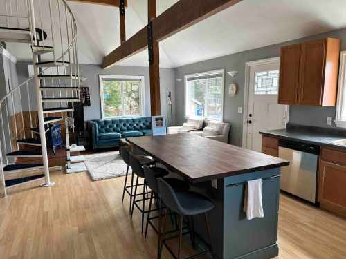 Modern open-concept living space featuring a kitchen island, spiral staircase, and cozy seating area with large windows.