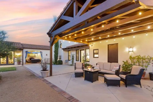 Cozy outdoor patio with seating, string lights, and a view of a landscaped yard at sunset.