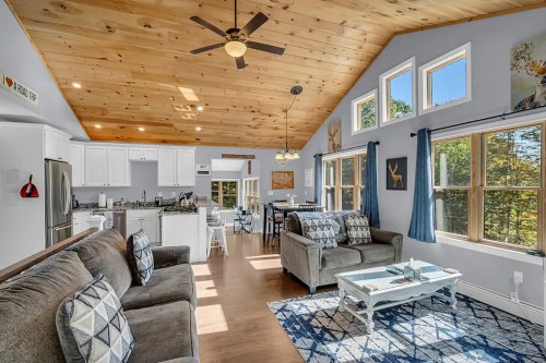 Cozy living area with a wooden ceiling, large windows, and modern furnishings, featuring a sofa and dining space.