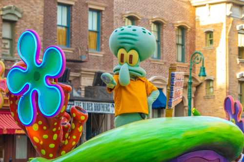 A green cartoon character with a yellow shirt stands on a colorful float during a parade, surrounded by vibrant decorations.