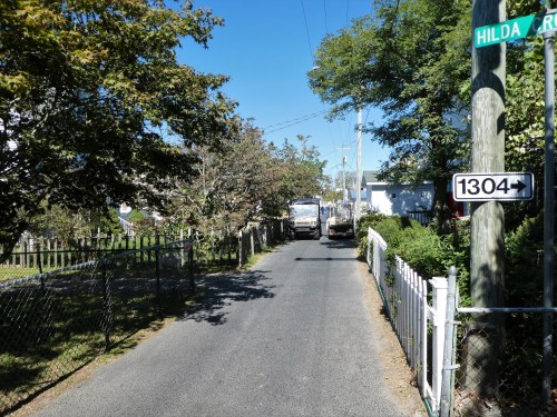 A narrow road lined with trees and fences, featuring two trucks and a street sign for Hilda Road.