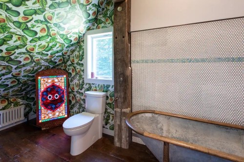 A unique bathroom featuring avocado-patterned wallpaper, a stained glass window, and a vintage metal bathtub.