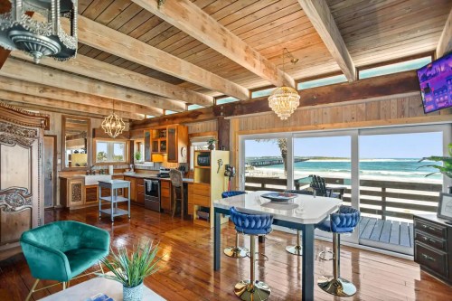 Bright beach house interior with wooden beams, modern kitchen, and ocean view through large windows. Cozy seating area included.