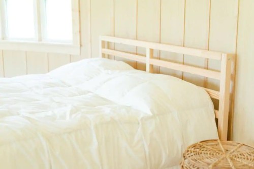 A cozy bedroom featuring a light wooden bed frame and a white comforter, with a woven basket beside it.
