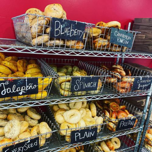 A display of various bagels in baskets, labeled with flavors like blueberry, cinnamon raisin, and jalapeño.