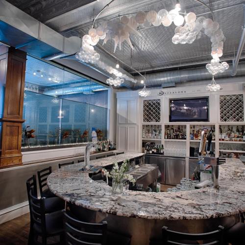 A stylish bar with a marble countertop, modern lighting, and a well-stocked back shelf in a contemporary setting.