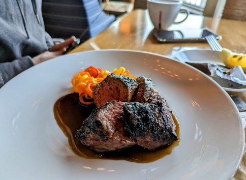 A plate featuring grilled steak with a dark crust, served with colorful spiral pasta and a sauce.