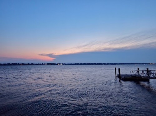 A serene lake at dusk, with soft blue and pink hues in the sky and a small dock extending into the water.