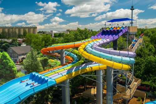 Colorful water slides twist and turn in a park, with people enjoying the ride under a bright blue sky.