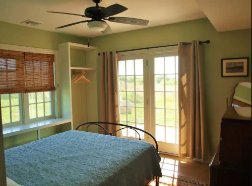 Cozy bedroom with a green wall, a bed, and large windows leading to a scenic outdoor view.