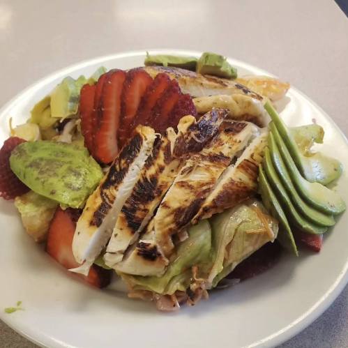 A plate of salad topped with grilled chicken, sliced strawberries, avocado, and mixed greens.