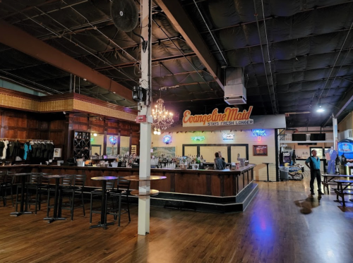 Interior of a bar with wooden decor, a chandelier, and a sign reading "OrangeLine Maid" in a spacious setting.