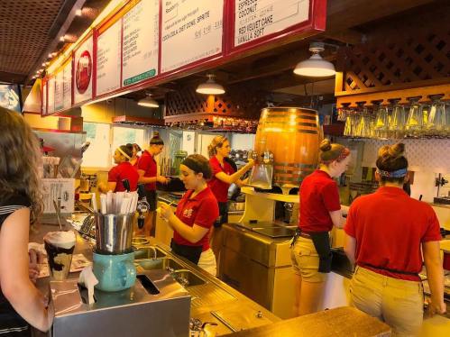 A busy ice cream shop with staff in red shirts serving customers and preparing desserts at the counter.