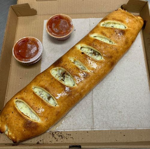 A large, golden-brown calzone with slits on top, served in a pizza box with two cups of marinara sauce.
