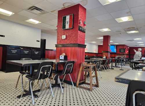 A spacious diner interior with red walls, black accents, and empty tables. A person stands in the background.