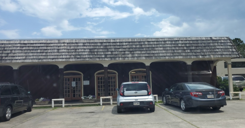 A building with a wooden roof and multiple doors, surrounded by parked cars in a lot under a cloudy sky.