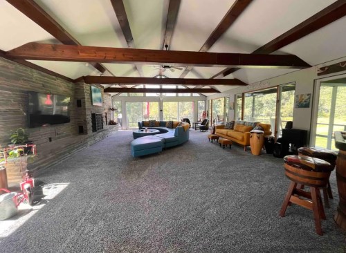 Spacious living room with high beams, large windows, colorful furniture, and a cozy carpeted area.