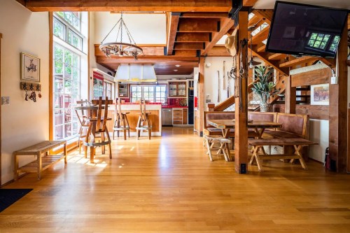 Bright, open kitchen and dining area with wooden beams, large windows, and rustic furniture.
