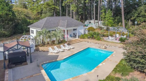 Aerial view of a backyard with a swimming pool, lounge chairs, and a house surrounded by trees and landscaping.