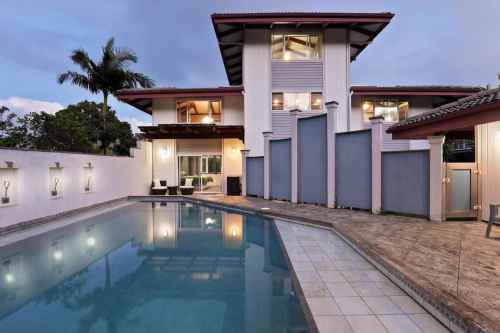 A modern house with a pool, surrounded by palm trees, under a twilight sky.
