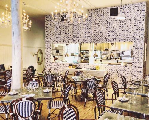 A stylish restaurant interior with wooden floors, patterned chairs, and a decorative wall, featuring an open kitchen.
