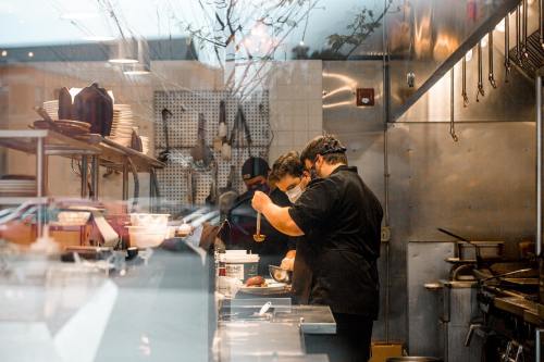 Two chefs in a restaurant kitchen prepare food, wearing masks and focused on their tasks.