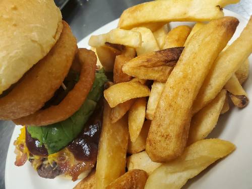 A juicy burger with onion rings, lettuce, and cheese, served with a side of golden French fries on a white plate.