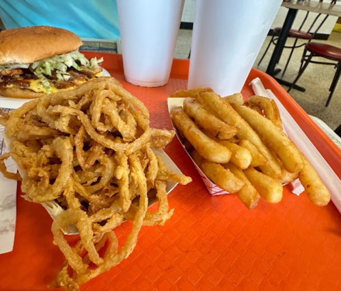 A tray with a burger, onion rings, and French fries, accompanied by two large drinks.