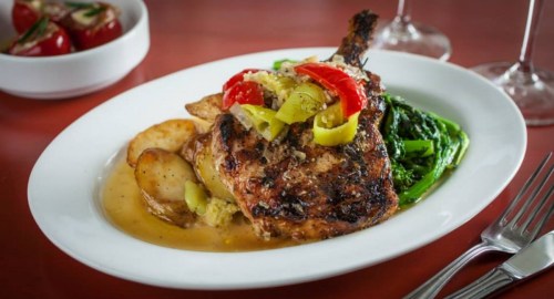 Grilled chicken with peppers, served with roasted potatoes and sautéed greens on a white plate.