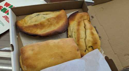 Three baked calzones in a pizza box, with one calzone slightly burnt and the others golden brown.