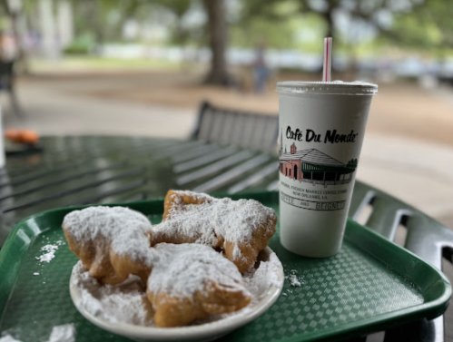 A plate of powdered sugar-covered beignets next to a Café Du Monde iced coffee on a green tray.