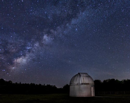 A dark sky filled with stars and the Milky Way, with a small observatory dome in the foreground.
