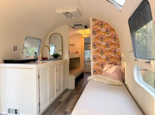 Interior of a cozy, modern camper with a kitchenette, a bed, and colorful wallpaper. Bright and inviting space.