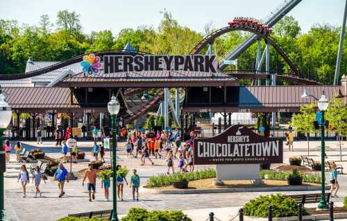 A bustling entrance to Hersheypark, featuring the ChocolateTown sign and visitors enjoying the park on a sunny day.