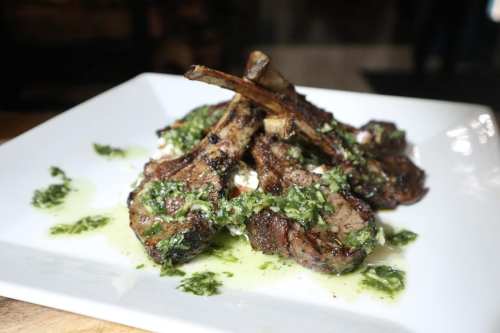 Grilled lamb chops topped with a green herb sauce, served on a white plate.