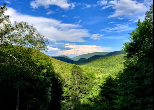 A scenic view of lush green mountains under a blue sky with scattered clouds.