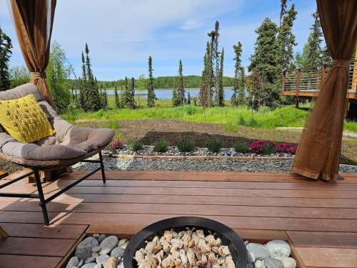Cozy outdoor seating area with a fire pit, overlooking a serene lake and lush greenery in a tranquil setting.