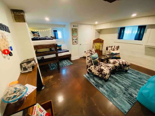 Cozy basement room with bunk beds, seating area, and colorful decor, featuring a blue rug and bright lighting.