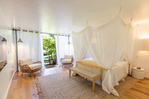 Bright, airy bedroom with a canopy bed, natural light, and minimalist decor, featuring wooden accents and a cozy rug.