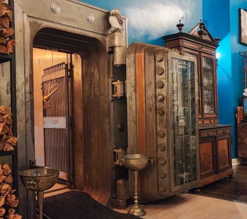 A vintage vault door stands open, revealing a secure room, with a wooden cabinet and decorative elements nearby.