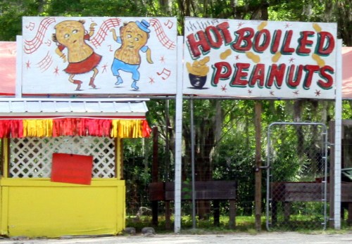 Colorful sign for "Hot Boiled Peanuts" featuring dancing peanut characters and a vibrant food stand.