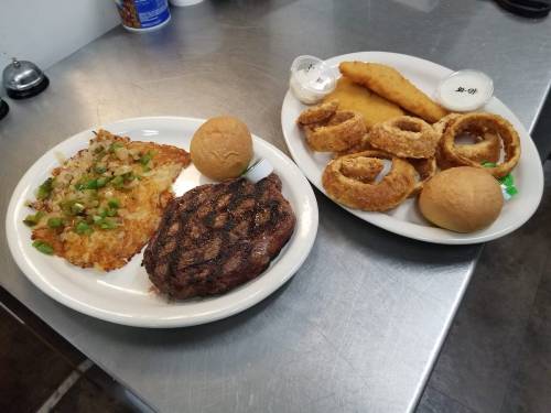 A plate of grilled steak with rice, green onions, rolls, and a side of onion rings and fish fillet.