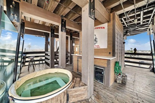 A rooftop space featuring a hot tub, wooden beams, and a bar area with stools, overlooking a scenic view.