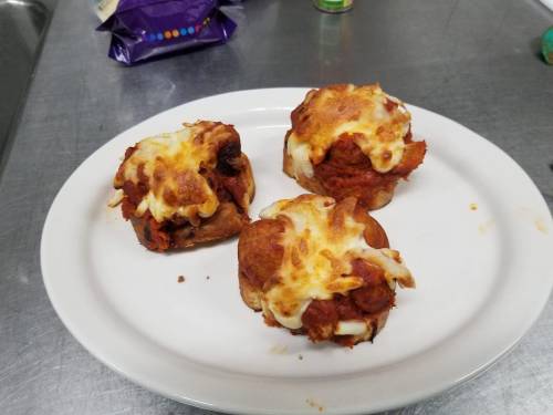 Three cheesy mini pizzas topped with sauce and meat on a white plate, set on a stainless steel surface.