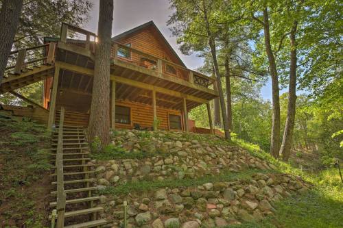 A log cabin nestled among trees, featuring a spacious deck and stone steps leading up to it.