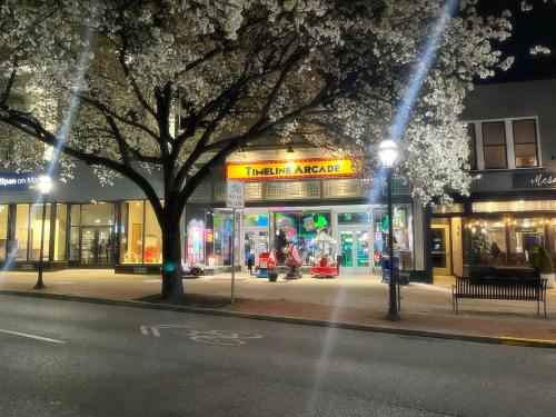 A brightly lit arcade named "Timeline Arcade" under blooming trees at night, with colorful games visible inside.