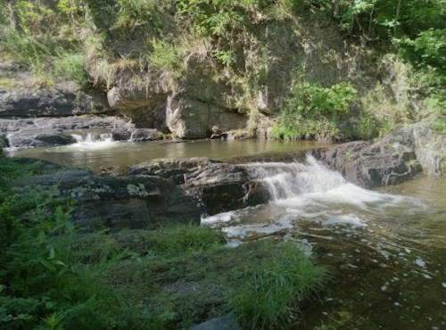 A serene river flows over rocks, surrounded by lush greenery and steep cliffs.